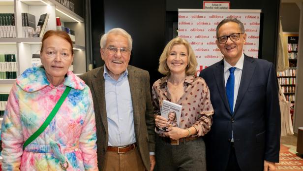 46-219680943 Vier Erwachsene stehen nebeneinander, eine Frau hält ein Buch und alle lächeln in einer Buchhandlung.