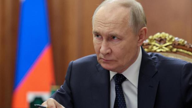 Russian President Vladimir Putin meets with Federal Customs Service Head Valery Pikalev in Moscow Putin sitzt an einem Tisch mit Papieren und einem Stift, im Hintergrund die russische Flagge.
