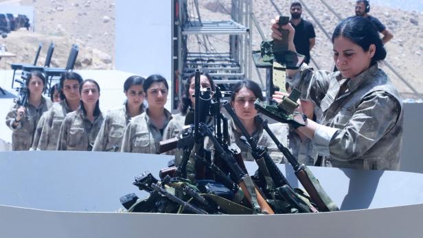 FILES-IRAQ-KURDS-TURKEY-CONFLICT Mehrere Frauen in Uniform legen Gewehre und Munition in einen Behälter, während andere in einer Reihe dahinter stehen.