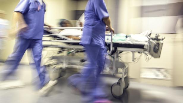 Ärzte in blauer Kleidung schieben eine Person auf einer Trage durch einen Flur.