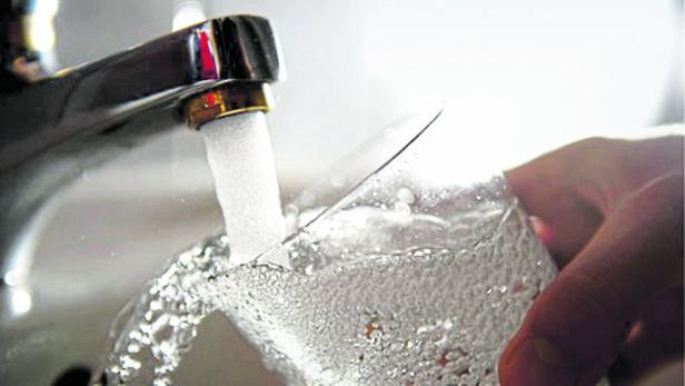 Wasser fließt aus einem Wasserhahn in ein Glas.