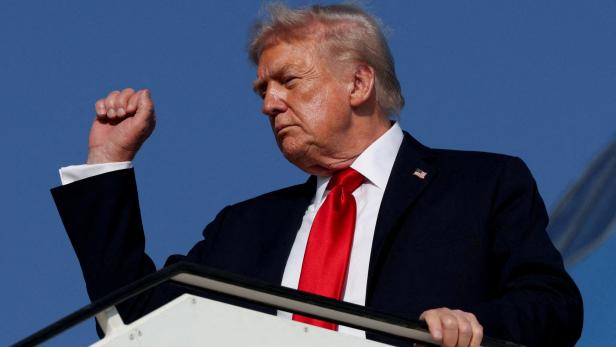 FILE PHOTO: U.S. President Trump boards Air Force One en route to Sharm El-Sheikh Donald Trump steht mit erhobener Faust vor blauem Himmel auf einer Treppe.