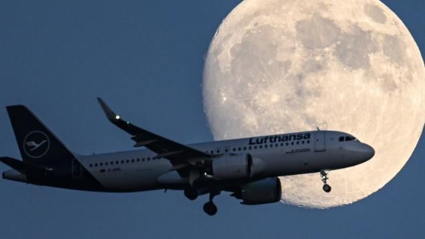 Mond in Hessen Ein Passagierflugzeug fliegt vor einem riesigen, hellen Vollmond am dunklen Himmel.