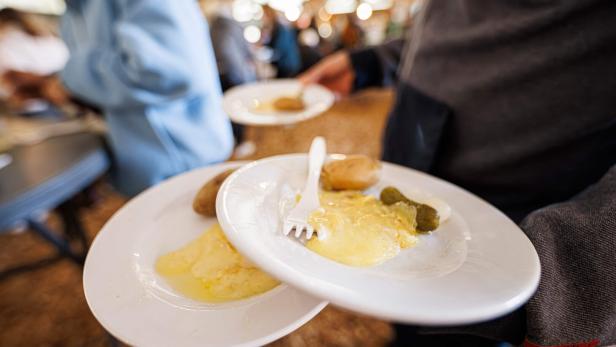 SWITZERLAND-FOOT-CULTURE-TRADITION-RACLETTE Zwei Teller mit geschmolzenem Käse, Kartoffeln und Essiggurken werden von einer Person getragen.