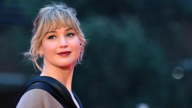 Jennifer Lawrence Jennifer Lawrence lächelt mit blonden Haaren und dunklem Lippenstift vor dunklem Hintergrund.