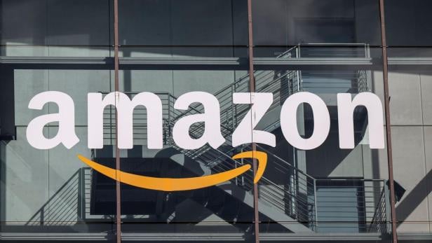Großes Amazon-Logo mit gelbem Pfeil auf einer Glasfassade, dahinter eine Metalltreppe und Schatten.
