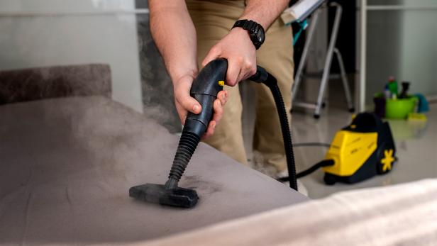 Amon Vertriebs GmbH: Der Dampfvollautomat für die Industrie ermöglicht eine effiziente, chemiefreie Reinigung in Profi-Bereichen. // Jemand stabsaugt ein Sofa.