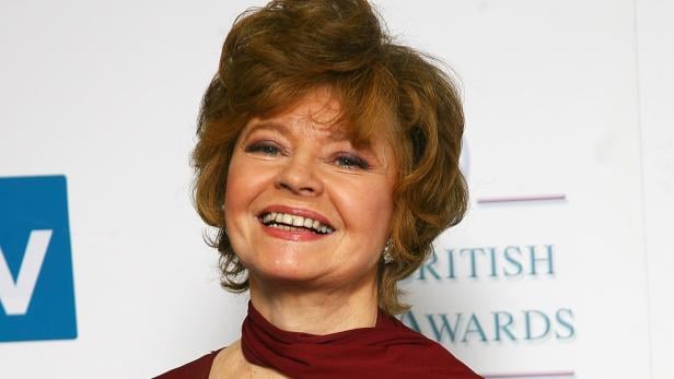 Prunella Scales in einem roten Kleid lächelt bei Veranstaltung.