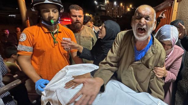 Palestinians carry a man, who according to medics was killed in an Israeli strike, at Nasser Hospital in Khan Younis Ein älterer Mann schreit verzweifelt, während mehrere Menschen, darunter ein Rettungshelfer, um einen mit Tuch bedeckten Körper trauern.