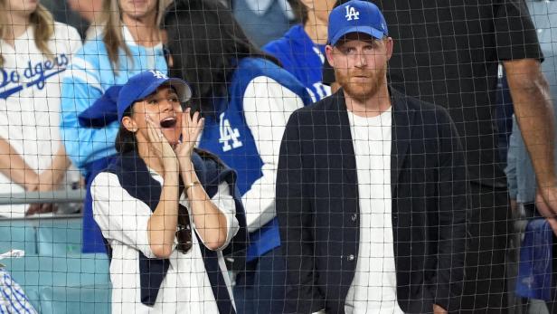 Meghan und Harry, beide mit "LA"-Kappen, schauen ein Baseballspiel an, Meghan jubelt.