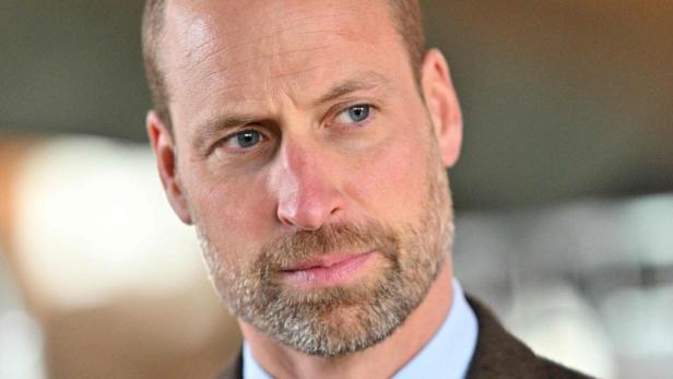 Prinz William mit Bart und braunem Sakko blickt zur Seite.