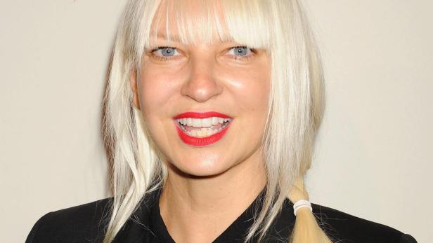 Sängerin Sia mit blondem Pony und schwarzem Blazer bei einem öffentlichen Auftritt.