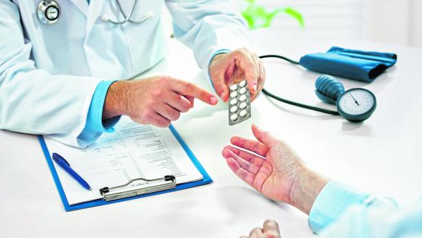 Ein Arzt in weißem Kittel reicht einem Patienten eine Blisterpackung mit Tabletten.