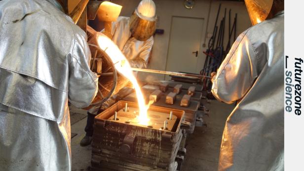 drei Menschen in silbernen Schutzanzügen gießen flüssiges Metall in eine Form