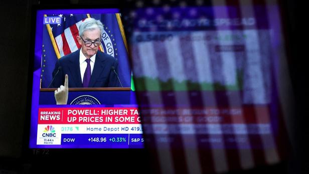 FILE PHOTO: A U.S. flag hangs in front of a screen that broadcasts a news conference by U.S. Federal Reserve Chair Jerome Powell as traders work on the floor of the NYSE in New York Auf einem Bildschirm ist Jerome Powell zu sehen, während CNBC über steigende Preise berichtet.