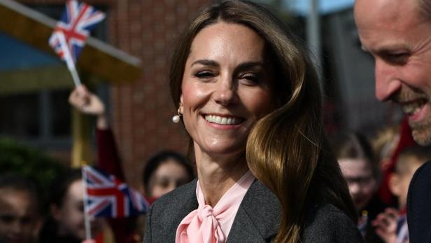 Kate, mit Blumenstrauß, lächelt neben William, während Kinder mit Union-Jack-Flaggen winken.