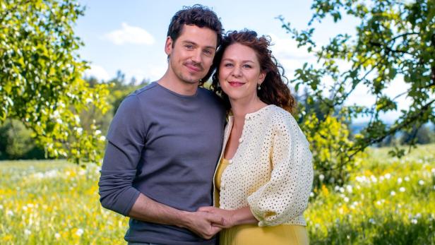 Mann und Frau stehen aneinandergeschmiegt auf einer Wiese unter Bäumen