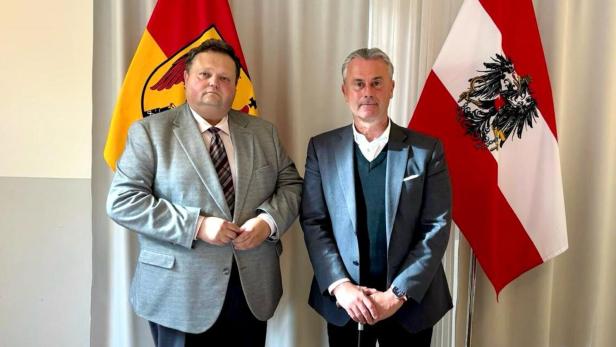 Norbert Hofer (FPÖ), re. und Bernd Strobl (ÖVP) Zwei Männer im Anzug stehen nebeneinander vor einer rot-gelben und einer rot-weiß-roten Fahne mit Adler.