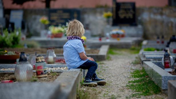 Little toddler boy, sitting on a grave in cemetery, sad and lonely, springtime Little toddler boy, sitting on a grave in cemetery, sad and lonely, springtime