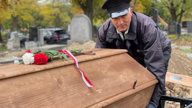 Ein Totengräber hebt einen Holzsarg mit Blumenschmuck in ein Grab.