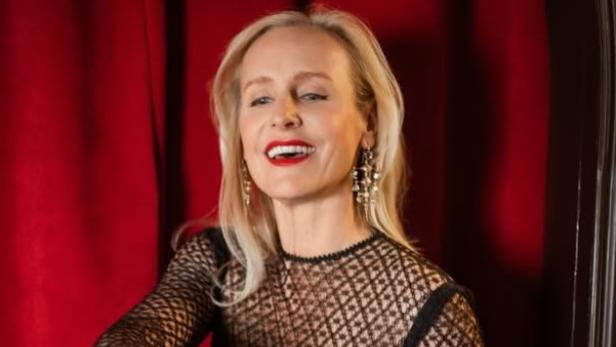 Frau in elegantem schwarzen Kleid schenkt Sekt in Gläser vor rotem Vorhang ein.