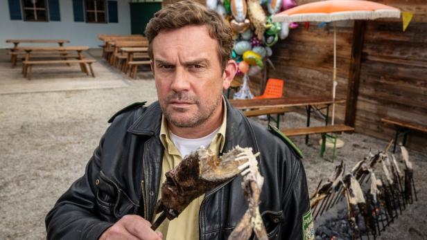 Sebastian Bezzel hält als Franz Eberhofer halbgegessenen Steckerlfisch hoch 