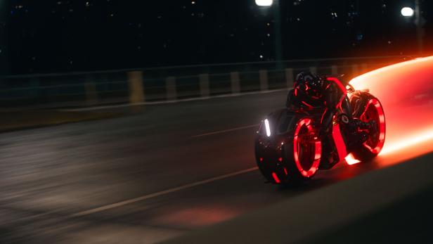 Ein Light Cycle aus dem Film Tron. Das Motorrad hat Räder ohne Speichen, ist rasant, der Fahrer verschmilzt damit und das Bike zieht einen Lichtstrahl hinter sich her.