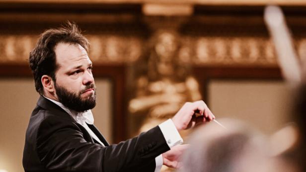 46-219863842 Ein Dirigent im Frack -Petr Popelka - leitet konzentriert ein Orchester in einem prunkvollen Konzertsaal.