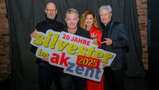 Vier Personen stehen zusammen und halten ein großes Schild mit der Aufschrift „20 Jahre Silvester im akzent 2025“.