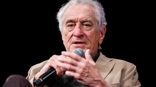 Robert De Niro Robert De Niro spricht in ein Mikrofon vor schwarzem Hintergrund.