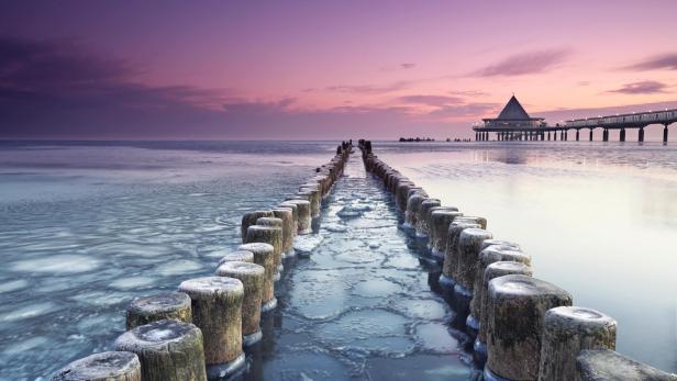 Ein Sonnenuntergang an einem Meer; mit Holzpfosten, die ins Wasser gehen