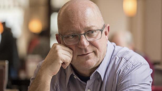 Ein kahlköpfiger Mann mit Brille stützt nachdenklich sein Gesicht auf die Hand.
