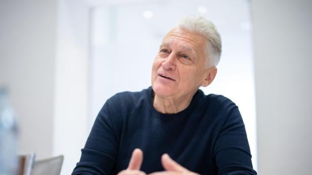 INTERVIEW MIT RAINHARD FENDRICH Ein Mann mit grauen Haaren und einem blauen Pullover sitzt an einem Tisch.