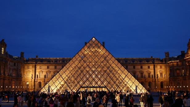 People walk near the glass Pyramid of the Louvre museum People walk near the glass Pyramid of the Louvre museum