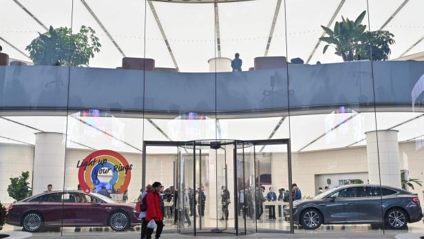 Großes, modernes Huawei-Geschäft mit Glasfassade, zwei ausgestellten Autos und mehreren Menschen im Inneren.