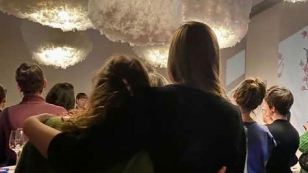 Menschen umarmen sich in einem stimmungsvoll beleuchteten Ausstellungsraum.