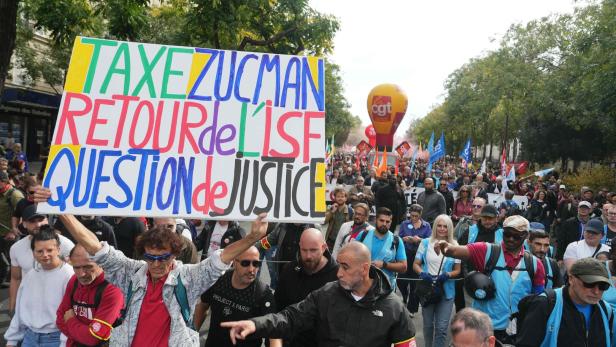 FRANCE-SOCIAL-STRIKE-UNIONS-DEMO Viele Menschen demonstrieren auf einer Straße, vorne wird ein großes, buntes Protestplakat mit politischen Forderungen hochgehalten.