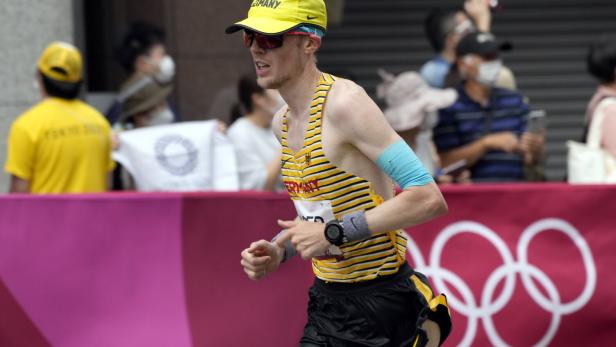 Olympic Games 2020 Athletics Richard Ringer mit gelber Kappe und Sonnenbrille läuft vor dem Hintergrund der Olympischen Ringe.