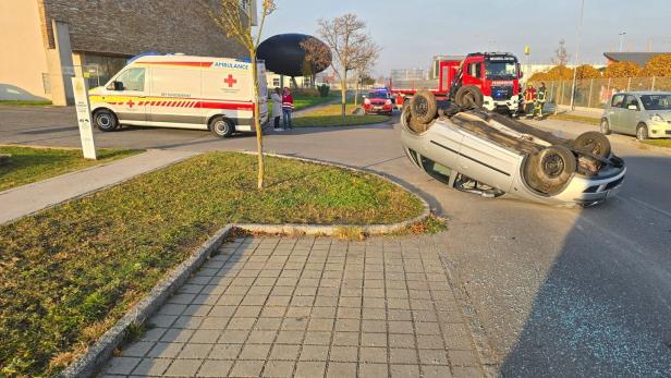 Ein Auto liegt auf dem Dach auf der Straße, während Rettungswagen, Feuerwehr und Polizei vor Ort sind.