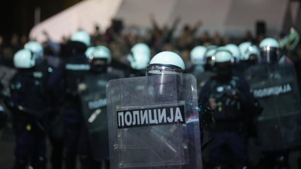 Mehrere Polizisten in Schutzkleidung und Helmen stehen mit Schilden vor einer Menschenmenge.