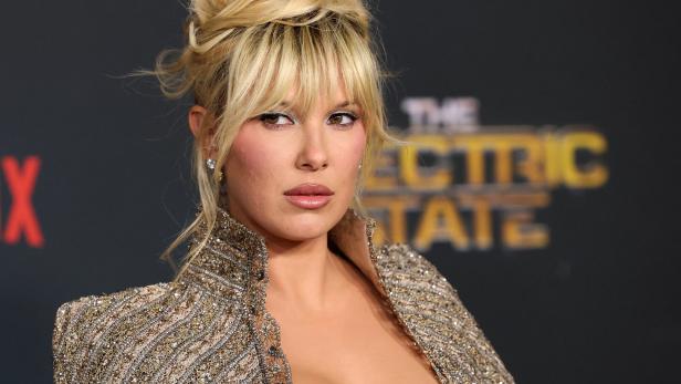 Millie Bobby Brown in einem goldenen Kleid blickt in die Kamera.