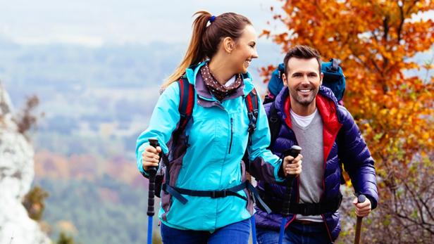 Ein Mann und eine Frau wandern in den Bergen, umgeben von herbstlich gefärbtem Gelände.