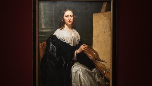 Porträt einer Frau, die eine Malpalette hält und vor einer Staffelei sitzt.