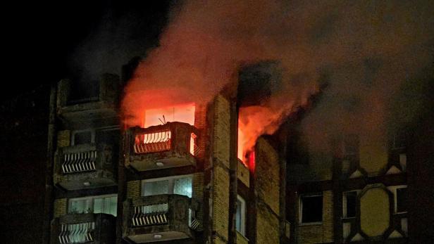 Aus den oberen Stockwerken eines Wohnhauses schlagen Flammen und dichter Rauch in die Nacht.