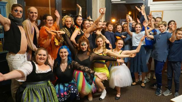 Eine große Gruppe von Menschen in bunten Kostümen und fröhlichen Posen, als ob sie gemeinsam feiern oder auftreten.