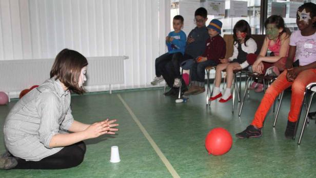 Eine Frau mit weißer Gesichtsbemalung führt einen Zaubertrick vor einer Gruppe von Kindern auf.