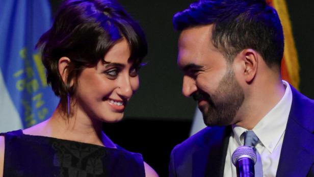 Rama Duwaji und Zohran Mamdani blicken sich vor Flaggen an.