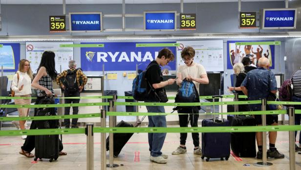 Reisende stehen mit Gepäck in einer Schlange vor den Ryanair-Check-in-Schaltern.