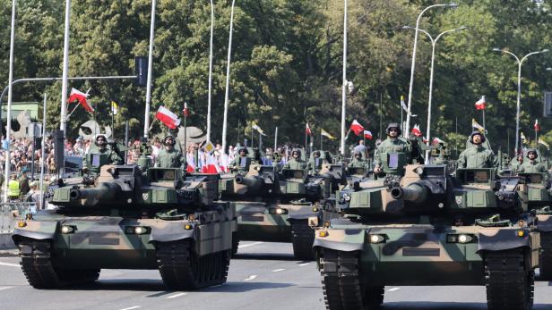 Mehrere Panzer mit Soldaten fahren auf einer Straße, umgeben von Menschen mit polnischen Fahnen.