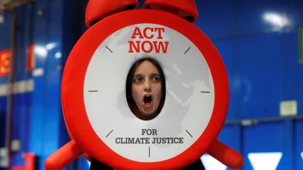 Eine Person schaut durch eine rote Uhr mit der Aufschrift "Act Now for Climate Justice".
